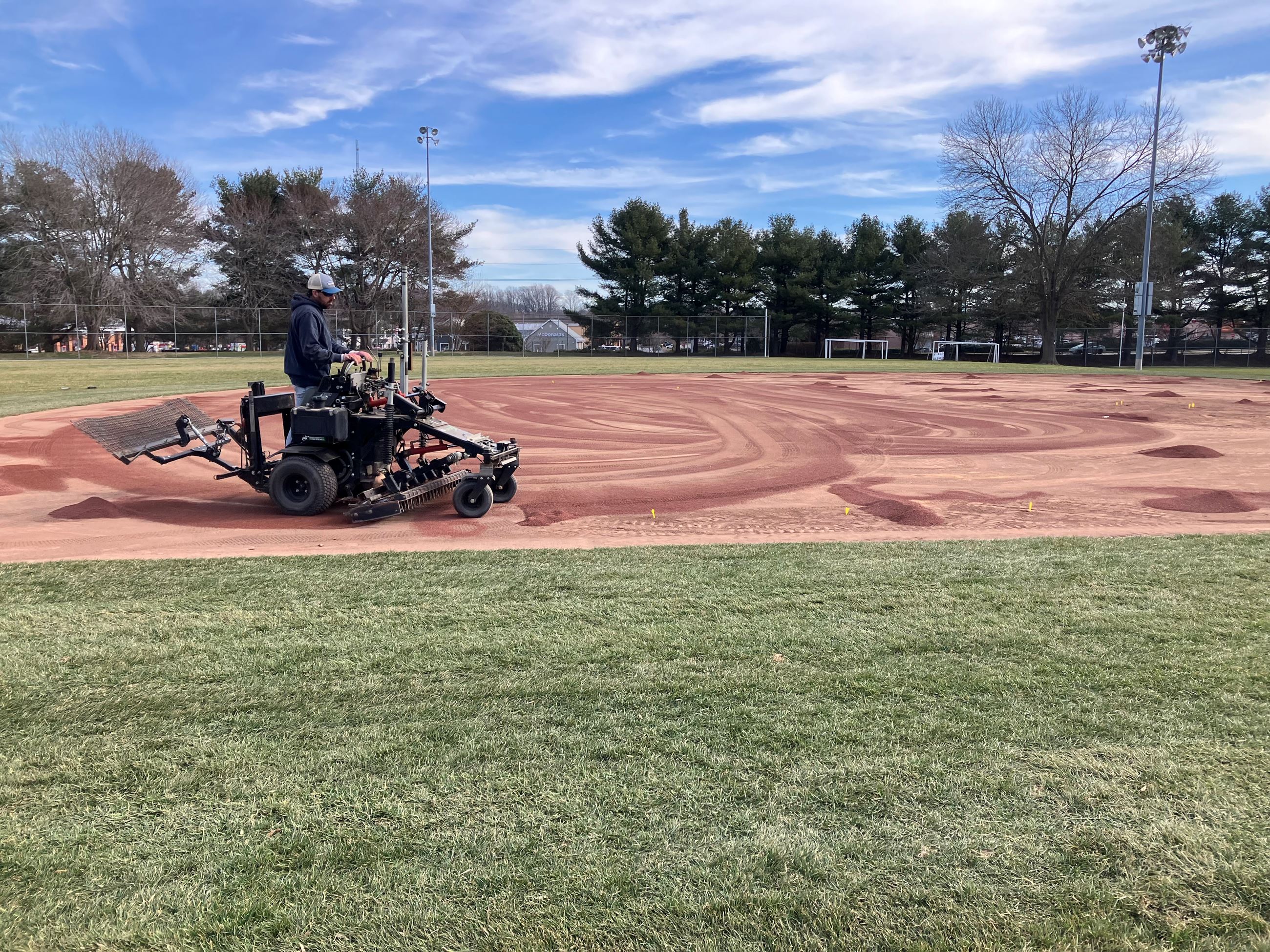 A worker upgrades and levels a baseball field with new infield mix